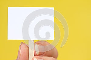 Hand Holding Tiny Sign on Yellow with Copy Space