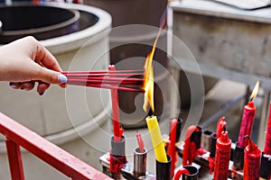 Hand holding to light the red incense with flame of candle in the temple