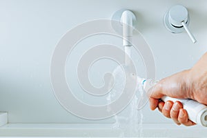 Hand holding a toothbrush under flowing water from faucet in a bathroom