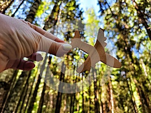 Hand holding toy wooden airplane plane and trees in forest background. Concept of flying on an airplane, travel, leisure