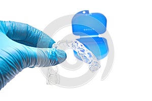 Hand holding transparent individual dental tray for teeth whitening in front of the dental container