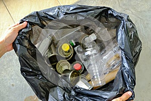 _Hand holding trash bag of unsorted plastic glass bottles metal cans containers paper cardboards collected for recycling. Zero