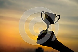 Hand holding trophy winner success with sunset