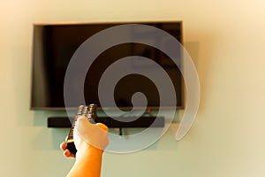 Hand holding TV remote control in front of widescreen TV set with blank screen.