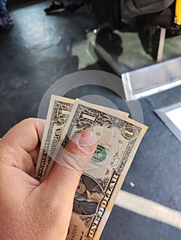 A hand holding two bills of one American dollar against the background of public transport. Selective focus