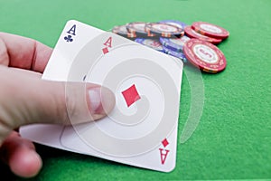 Hand holding two playing cards with aces on poker chips on a green table