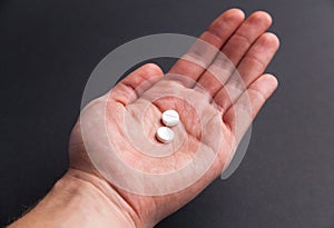 Hand holding two white pills on black background medicine pharmacy health