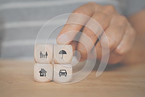 Hand holding umbrella icon on wooden cube block over family, vehicle and house symbol for health, property ,life, family