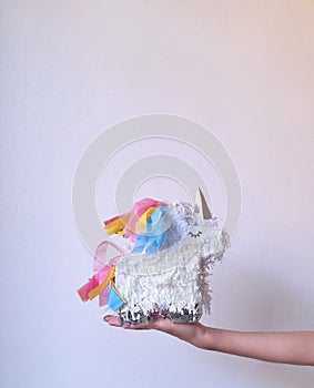 hand holding unicorn piñata against wall with space for text