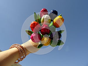 Hand Holding Up a Bouquet of Colorful Wooden Tulips agaist the background of the Blue sky