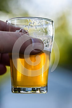 Hand holding up craft beer flight sample glass in sunlight outside