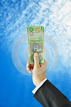 Hand holding up money - Australian dollars - on blue sky background