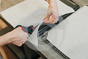 Hand holding up a sheet of baking paper and cut using a pair of scissors