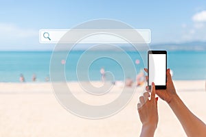 Hand holding up a smart phone at beach. Sea, sand and sky on the background. Sign of searching. Concept of modern technology and