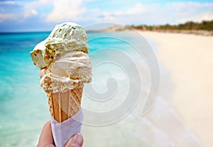 Hand is holding the vanilla ice cream. In the background is blue sky, sea nd sandy beach. This is situated in tropical resort