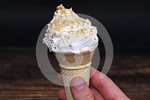 Hand holding a vanilla ice cream cone with caramel butterscotch nuts topping  on black background