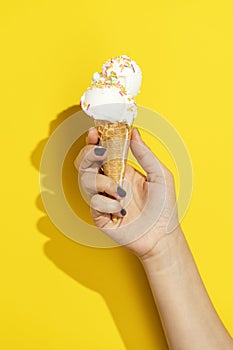 Hand holding vanilla ice cream cone on yellow background