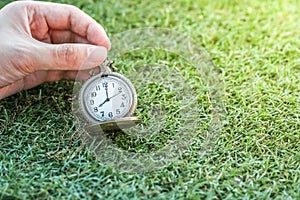 Hand holding vintage pocket gold watch with green grass, abstract for time concept with copy space