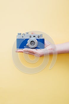 Hand holding vintage style camera on yellow background