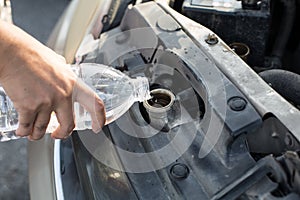 Hand holding water bottle is pouring water into the car radiator