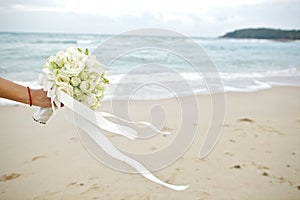Hand holding wedding bouquet with beach background