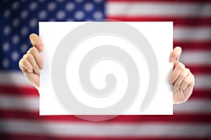 Hand holding white blank paper sheet mockup with US flag blurred