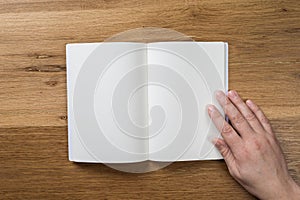 Hand holding white blank paper sheet mockup on wooden background
