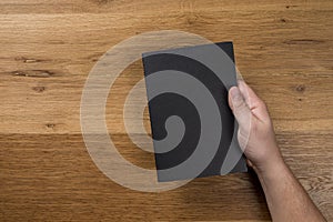 Hand holding white blank paper sheet mockup on wooden background