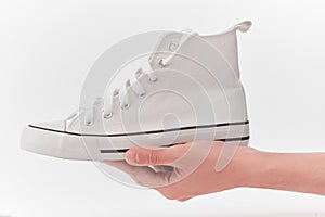Hand holding a white canvas sneaker on white background
