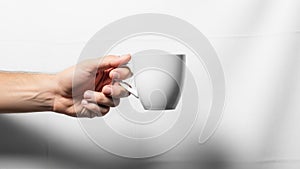 A hand is holding a white ceramic cup against a plain white background