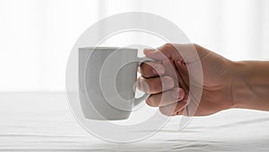 A hand holding a white ceramic mug against a plain background