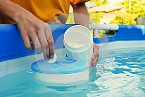 Hand holding white chlorine tablets over swimming pool skimmer. Chlorination of water in pool for disinfection and photo