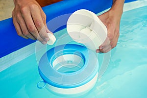 Hand holding white chlorine tablets over swimming pool skimmer. Chlorination of water in pool for disinfection and