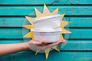 Hand holding white containers, turquoise background, styrofoam vessels, pop of yellow, casual indulgence