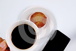 Hand holding a white cup of coffee, espresso, italian coffee with cupcake and smartphone on the white background, drink coffee,