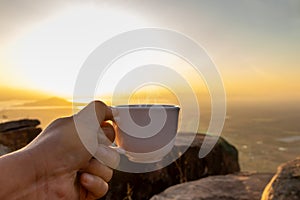 Hand holding a white cup of hot espresso coffee mugs and nature view of the sun background in the morning with sunlight