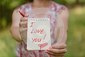 Hand holding white heart paper with I love you text on blur green grass background