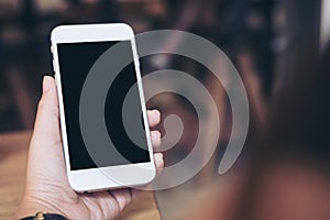 Hand holding white mobile phone with blank black screen in modern restaurant