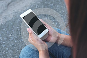 Hand holding white mobile phone with blank black screen while sitting on the street