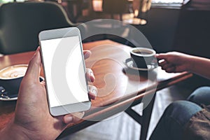 Hand holding white mobile phone with blank screen with woman drinking coffee in modern cafe