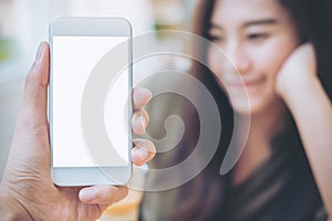 Hand holding white mobile phone with blank white screen and blur smiley woman face background in modern cafe