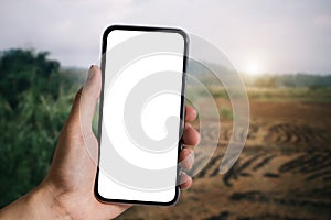 Hand holding white mobile phone with blank white screen in forest