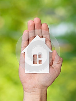 Hand holding white paper house figure on green background