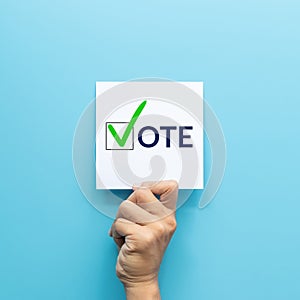 Hand holding white paper with the `vote` and green check mark voting symbols in checkbox of the inscription isolated on blue photo