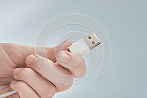 Hand holding white USB cable  on gray background