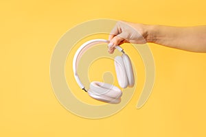 Hand holding white wireless headphones against yellow background