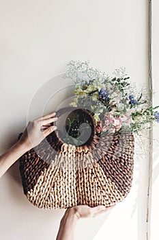 hand holding wildflowers in wicker bag at rustic window. colorful flowers in brown basket in sunlight, space for text. rural