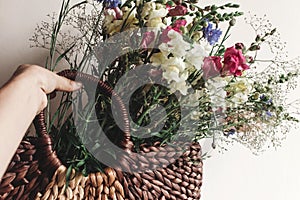 hand holding wildflowers in wicker bag at rustic window. colorful flowers in brown basket in sunlight, space for text. rural
