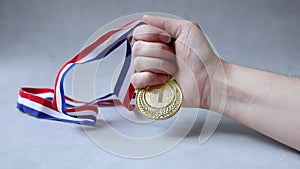Hand holding winner or champion gold trophy medal on concrete stone grey background. Victory first place of competition