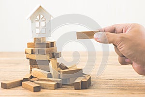 Hand holding wood block with model white house on wood block game. Investment risk and uncertainty in the real estate housing mark